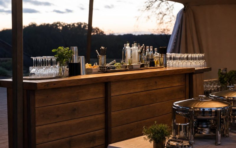Portable event bar and stainless catering chafing dishes set up under a tent by Creative Events & Rentals